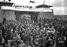 Foule de prisonniers saluant des soldats américains sur un char devant la porte d'entrée du camp de Mauthausen en mai 1945.