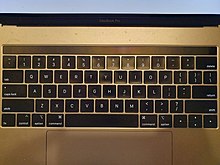 2018-as MacBook Pro 15 inch billentyűzete. A Touch Bar csíkja a felső sötét csík (mert a Mac ki van kapcsolva).