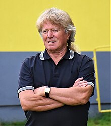 Viktor Sodoma wearing dark polo shirt, standing with arms crossed, squinting to the right of camera