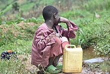 Ein Kind sitzt an einer Wasserstelle in der Hocke. Ein Wasserkanister steht vor ihm.