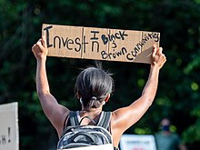 Protester holding a sign in Brooklyn: "Invest in black and brown communities" George Floyd protest in Grand Army Plaza June 7 (73227).jpg
