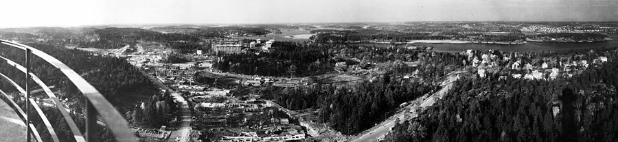 Vy mot sydväst och norr över Bredäng och del av Mälarhöjden från Sätra radiolänktorn 1963. Längst till vänster syns en del av länktornets räcke, i bildmitt pågår byggarbetena för Bredäng och intill ligger Jakobsbergs gård. I bakgrunden längst till höger skymtar Höglandet.