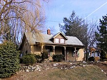 A medium size 2-story house sits on a small hill. Trees surround the house