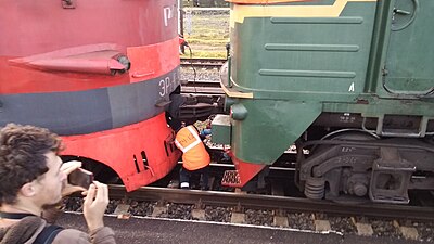 The driver is connecting brake-air supply hose, a railfan is documenting that