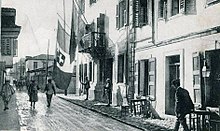 Italian soldiers in Vlore, Albania during World War I. The tricolour flag of Italy bearing the Savoy royal shield is shown hanging alongside an Albanian flag from the balcony of the Italian headquarters. Vlora zur Zeit der italienischen Besatzung 1916-1920.jpg