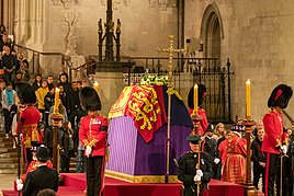 Elizabeth II lying in state in a coffin draped with the royal standard.