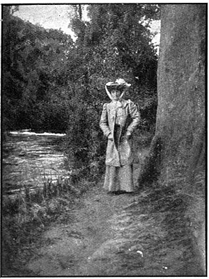 Lady standing beside a large tree on a track next to a river surrounded by bush