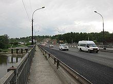 Photographie prise sur le trottoir d'un pont (sur la rivière Inia), avec des véhicules circulant dans la direction du photographe. Les véhicules dans l'autre sens sont sur un autre pont parallèle en arrière-plan. Au fond se trouve une colline recouverte d'arbres.