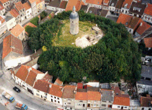 An aerial colour photograph of stone-built tower on a grassy and wooded mound, surrounded by houses