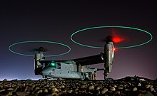 Ground crew refuels an MV-22 before a mission in central Iraq at night. The rotors are turning and the tips are green, forming green circles.