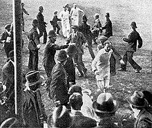 A cricketer leading his team off the field watched by a crowd