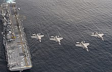 Four Marine Corps F-35B Lightning II stealth fighters flying over the USS America (LHA-6) Four F-35B Lightning II aircraft perform a flyover above the amphibious assault ship USS America (LHA 6) during the Lightning Carrier Proof of Concept Demonstration (30357956614).jpg