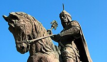 A stone statue of a man in warrior clothes on horseback.