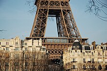 photographie du bas de la tour Eiffel avec quelques immeubles en premier plan
