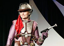 Femme en armure et en tenue violette avec un pistolet.