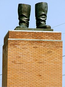a tan brick pedestal supporting a pair of bronze statue boots with nothing attached