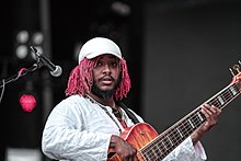Picture of Thundercat, who looks at the camera while he plays a bass guitar.