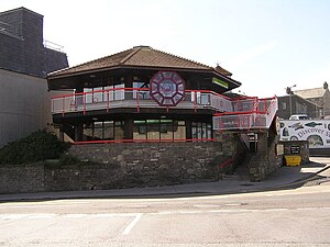 A two-storey hexagonal building on a stone retaining wall, with tiled roof, with a Chinese motif on the upper balcony