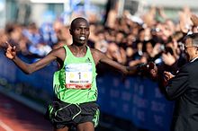 Photo of Wilson Chebet holding his arms wide with an audience behind fences