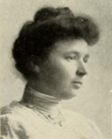 A young white woman in 3/4 profile, dark hair in a bouffant updo, wearing a high-collared white blouse