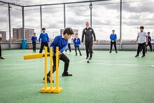 A boy striking a cricket ball on the rooftop of a school