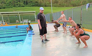 Swimmers in competitive swimwear perform squats prior to entering the pool in a U.S. military base, 2011. Participants with the Water Warrior class perform squats prior to entering the pool at Camp Foster, Okinawa, Japan, July 6, 2011 110706-M-VD776-004 (cropped).jpg