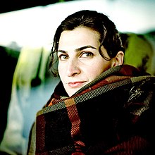 Pelin Esmer 2019. Junge türkische Frau mit durchdringendem Blick und einem hoch gewickelten Schal. Eine einzelne Haarsträne hängt ihr über die Schläfe.