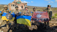 Cinq hommes en uniforme militaire tenant deux drapeaux ukrainiens et un drapeau de l'unité, devant les ruines d'une église.