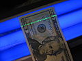 The security strip in a twenty-dollar bill glows green under a blacklight.