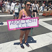 Woman caring a sign that reads Abolish ICE