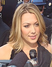 A portrait of Colbie Caillat, a blond woman speaking on a microphone