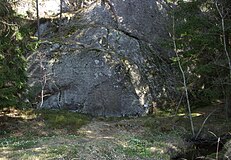 Runhällens placering i terrängen. Den gamla vägbanken stryker tätt förbi berget och i förgrunden till höger syns bäcken.