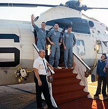 Photographie couleur des trois hommes d'Apollo 10 sortant d'un hélicoptère posé sur un porte-avions.