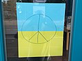Ukrainische Flagge mit handgemaltem Friedenszeichen (Peace) am Ladenfenster