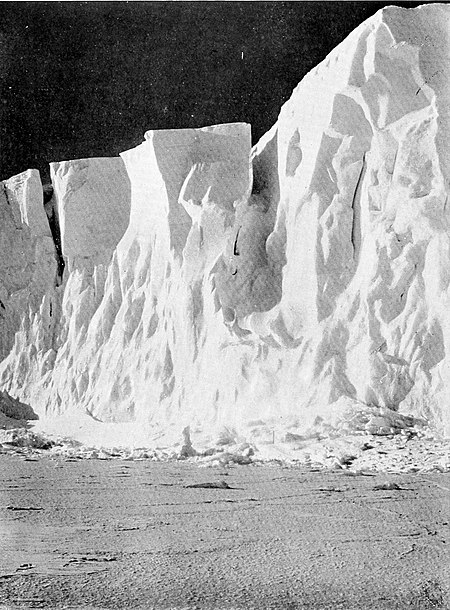 Photograph of craggy ice cliff rising from smooth sea ice