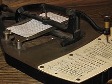 Un poinçon au-dessus d'un plateau de carte à perforer et une visée fixés aux extrémités d'un pantographe permettant de cibler les trous d'un clavier