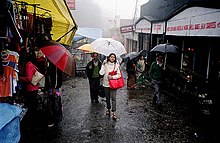 A few people walking on a wet street holding umbrellas. There are shops on either side of the street.