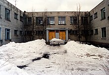 The front of a brown building where the ground is covered in dirty snow.