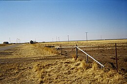 Een uitzicht over een veld in West-Oklahoma, met een aantal gebroken funderingen en graanopslagbakken.