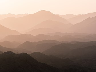 Montanhas Hajar ao amanhecer, Emirados Árabes Unidos. Acredita-se que as Montanhas Hajar tenham se formado pela primeira vez na convergência das placas Arábica e Eurasiática como resultado da mudança do continente euroasiático que ocorreu aproximadamente 30 milhões de anos atrás. Mais tarde, os beduínos se estabeleceram em diferentes áreas e fundaram comunidades pastoris escassamente povoadas em partes da cordilheira durante os tempos pré-islâmicos. Elas formam a cordilheira mais alta no leste da Arábia. Também conhecidas como “Montanhas de Omã”, separam a baixa planície costeira de Omã do alto planalto do deserto, e ficam a 50–100 km do Golfo de Omã. (definição 5 184 × 3 888)