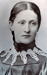 Photo en noir et blanc d'une jeune femme au visage ovale, avec un vêtement orné de dentelles blanches.