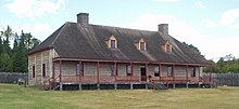 A large, rustic building sitting in a green field with a wooden fence and a forest in the background.