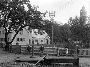 Fotografi över Ronneby stads elverk från tidigt 1900-tal med Gamla vattentornet i bakgrunden. Fotografi ur Blekinge museums samlingar.