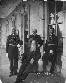 Three men in military uniforms standing around seated man