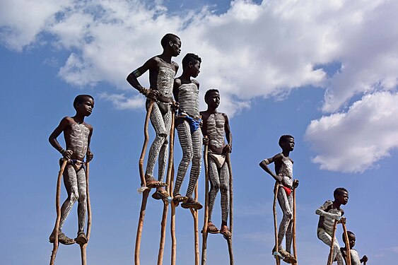 „Banna children in Ethiopia with traditional body painting, playing on wooden stilts“ von WAVRIK, CC BY-SA 4.0