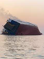 View of MV Golden Ray at sunrise following her capsizing on September 8, 2019. The ship is viewed from the stern, with the starboard side completely out of the water but not completely resting on her port side yet.