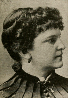 19th-century B&W portrait profile photo of a woman with her hair in an up-do, wearing a dark, high-collared blouse.