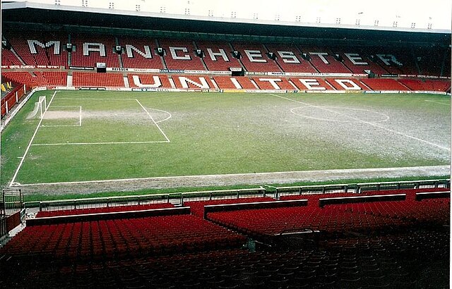 Tribune d'un stade de football avec des sièges rouges sur laquelle est inscrit : « Manchester United »