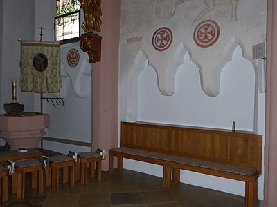 Photographie d'un banc de bois placé devant une triple niche creusée dans le mur d'une église.