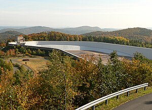 Blick von der Aussichtsplattform Peterskopf am Oberbecken II (auf dem Ermerod) etwa nach Südosten zum leeren Oberbecken I (mit Einlaufbauwerk; auf dem Peterskopf) der Pumpspeicherwerke Waldeck mit Bergen des Kellerwaldes im Hintergrund